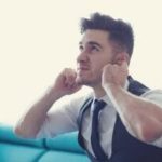 Man in a suit covering his ears, expressing discomfort, possibly related to noisy water heater issues discussed in plumbing maintenance context.