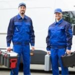 Two plumbers in blue uniforms holding toolboxes, standing in front of a service van, representing Carmine's Plumbing, Heating & Air Conditioning services in Danbury, CT.