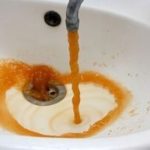 Rusty water flowing from a faucet into a sink, indicating potential issues with a water heater and the need for plumbing inspection.