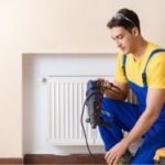 HVAC technician in blue overalls inspecting a heating radiator, emphasizing safety and professionalism in home service.