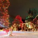 Nighttime view of brick house and trees decorated with red, green and white holiday lights with snowman figure and snow-covered ground