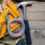 Hammer, pliers, measuring tape, and wire on wooden surface, representing essential tools for HVAC and plumbing work at Carmine's Plumbing, Heating & Air Conditioning.