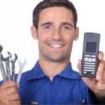 Plumber in blue uniform holds wrenches and smartphone, representing Carmine's Plumbing, Heating & Air Conditioning services.