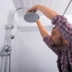 Man installing or adjusting a showerhead, demonstrating plumbing maintenance related to water flow and temperature control.