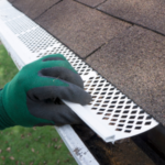 Person installing gutter guard on a roof, demonstrating a solution for preventing debris buildup in gutters.