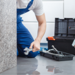 Plumber in blue overalls using a wrench near a water heater, emphasizing professional plumbing services and maintenance.
