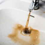 Brown water flowing from a faucet into a sink, highlighting potential plumbing issues and the importance of professional water heater maintenance.