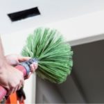 Person holding a green air duct cleaning brush, preparing to clean air vents for improved HVAC efficiency and air quality.