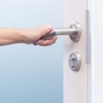 Hand grasping a modern door handle, symbolizing home access and maintenance for air conditioning efficiency.