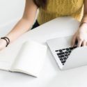 Person with long hair in a yellow sweater working on a laptop at a desk, with a notebook nearby for maintenance tips.