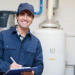 Plumber smiling while inspecting a water heater, representing Carmine's Plumbing, Heating & Air Conditioning services for efficient home maintenance in Danbury, CT.