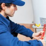 Plumber inspecting a water heater with tools, emphasizing maintenance for efficient plumbing services by Carmine's Plumbing, Heating & Air Conditioning in Danbury, CT.