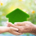 Child's and adult's hands holding a green house symbol, representing eco-friendly home solutions by Carmine's Plumbing.