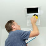 Man inspecting and cleaning a ceiling air vent, emphasizing HVAC maintenance for improved air quality in homes.