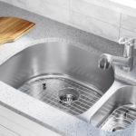 Stainless steel kitchen sink with a modern faucet and a wooden cutting board, illustrating plumbing maintenance and potential clogging issues.