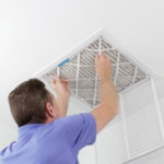 Technician replacing air conditioning filter in ceiling vent for HVAC maintenance.