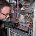 Technician repairing furnace electrical panel with tools, displaying intricate wiring for HVAC by Carmine's Plumbing.
