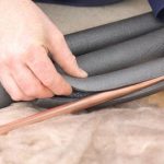 Person applying insulation to copper pipes, demonstrating winterization techniques for plumbing maintenance.