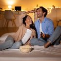 Couple enjoying a movie night on the floor with popcorn and remote control, highlighting home comfort and connection.