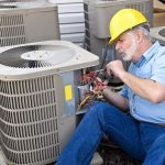 HVAC technician in yellow hard hat servicing air conditioning unit, emphasizing professional AC maintenance and repair services.