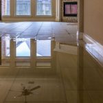 Flooded interior space with standing water on tiled floor, reflecting windows and ceiling fan, emphasizing plumbing maintenance importance.