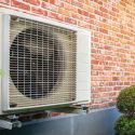 Air conditioning unit on a brick wall with green leaves and shrub, showcasing HVAC functionality for home comfort.