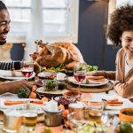 Smiling couple enjoying a festive meal with a roasted turkey and vegetables on a beautifully set dining table, celebrating togetherness and gratitude.