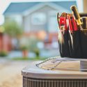 Air conditioning unit next to an organizer filled with colored pens and markers, set against a house and greenery background.