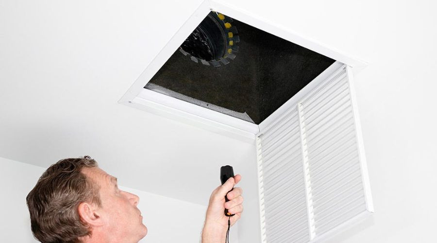Man inspecting a ceiling access panel for HVAC maintenance at Carmine's Plumbing and Heating services.