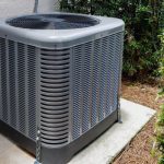 Air conditioning unit situated on a concrete pad, surrounded by greenery, emphasizing the importance of regular HVAC maintenance for efficiency and longevity.