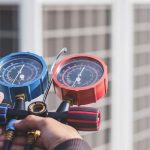HVAC technician holding refrigerant pressure gauges, essential for diagnosing bubbling sounds and refrigerant leaks in air conditioning systems.