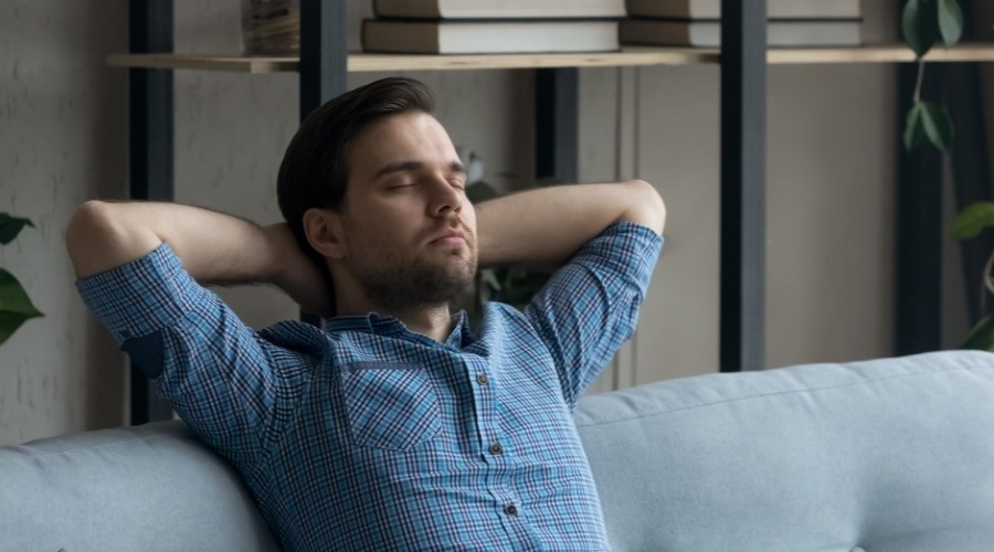 Man relaxing on a couch with hands behind his head, representing comfort and stress relief, relevant to home maintenance and HVAC service benefits.