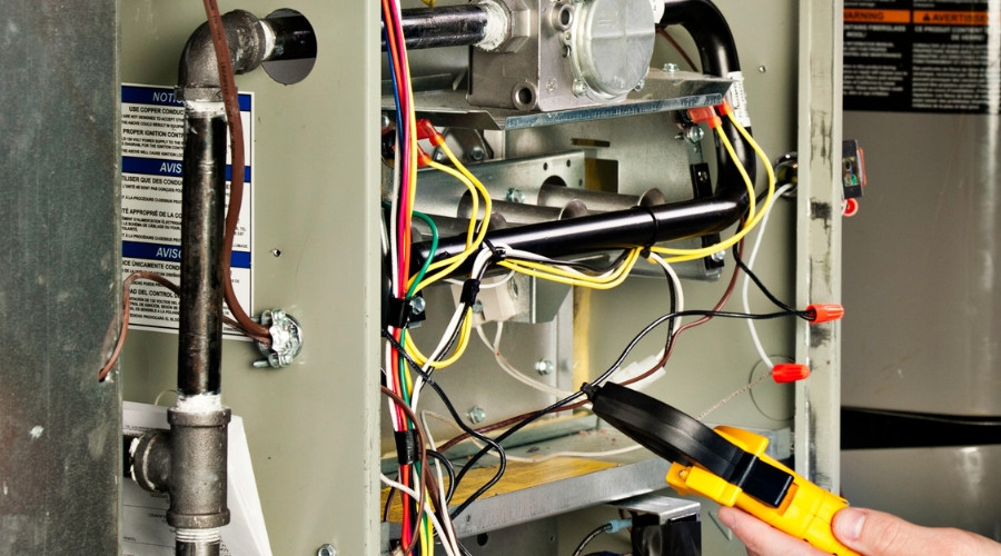 HVAC technician inspecting a furnace's wiring and components with a multimeter, emphasizing heating system maintenance and repair services.