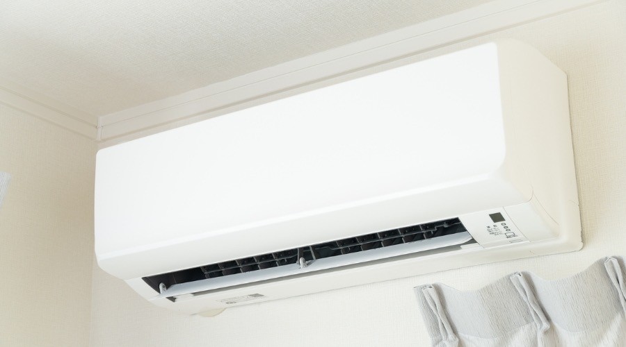 Indoor ductless mini split AC unit mounted high on interior wall near ceiling with horizontal vent and control panel visible